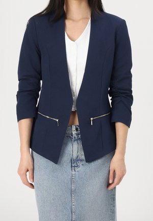 Námořnický blazer s upraveným střihem, dvěma zipovými předními kapsami a tříčtvrtečními rukávy, spárovaný s bílým ribbovaným topem a džínovou sukní.