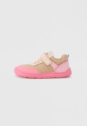 Chaussure de sport rose et beige avec une bride à velcro, tissu texturé, semelle rembourrée et semelle extérieure en caoutchouc. Présente des détails de couture sur les côtés.