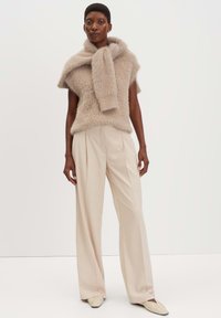 Beige, fluffy gebreid top met korte mouwen en een sjaalachtige kraag, gecombineerd met high-waisted, wijde crèmekleurige broeken. Platte, gestructureerde schoenen.