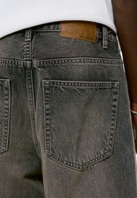 Sivi traperice s lagano istrošenom teksturom, koje imaju smeđi kožni detalj s oznakom "PULL&BEAR" na pojasu i dva stražnja džepa.