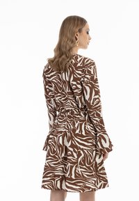 Hnědo-bíl dress s zebřími pruhy, dlouhými rozšířenými rukávy, elastickým pasem a délku ke kolenům. Hladká textura látky.