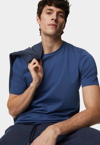 Blauwe T-shirt met korte mouwen van zachte stof, met een ronde halslijn. Het model houdt een donkerblauwe trui over één schouder.