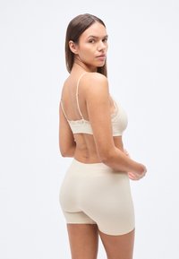 Μπεζ απαλό σουτιέν χωρίς ραφές με δαντέλα και ρυθμιζόμενες τιράντες, συνδυασμένο με κορυφαίο σορτσάκι με ψηλή μέση, που δείχνει λεία υφή υφάσματος και μινιμαλιστικό σχέδιο.