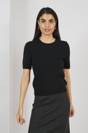 Maglia nera a maniche corte in maglia con scollatura rotonda, caratterizzata da una texture morbida e da un design aderente, abbinata a una gonna a quadretti.
