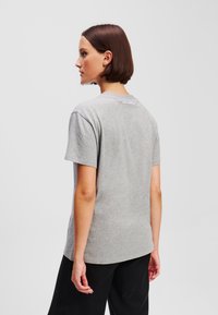 Grijze katoenen T-shirt met korte mouwen, ronde hals en een logodetail aan de achterkant. Soepele textuur, casual pasvorm, gedragen met zwarte broek.
