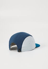 Tofarget cap med marineblå front og lyseblå bak, med buet skjerm og glidelåsdetalj bak for justerbar passform.