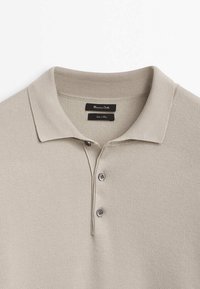 Polo en maille beige clair avec un col côtelé et trois boutons sur le devant, étiquette de marque à l'intérieur du col.