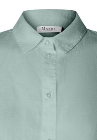 Camicia in lino verde chiaro con colletto a punta, sei bottoni sul davanti e etichetta "Maerz Muenchen". Tessuto testurizzato.