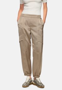 Beige satin cargo pants with elastic waistband, side pockets, and tapered cuffs, paired with patterned sneakers.