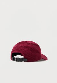 Boné de corduroy bordô com aba curvada, faixa ajustável preta na parte de trás e ilhós de ventilação nas laterais.