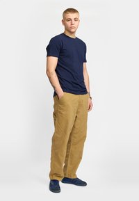 T-shirt di cotone blu navy, pantaloni in velluto a coste color sabbia e scarpe da ginnastica blu. Design semplice con maniche corte e scollatura tonda.