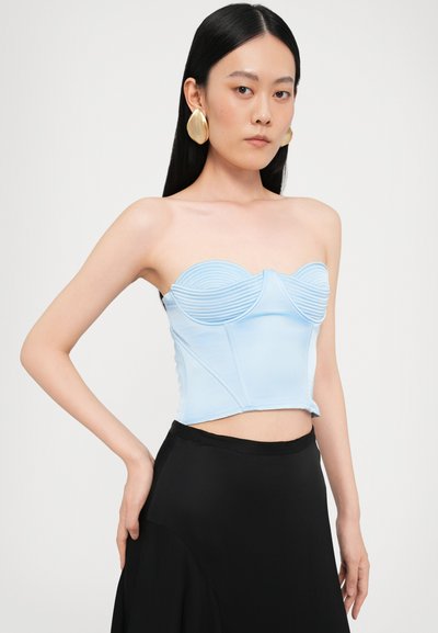Top sin mangas de color azul claro con textura acanalada, escote corazón y corte estructurado. Se lleva con una falda negra fluida.