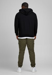 Black hooded sweatshirt with a regular fit and ribbed hem, paired with green cargo pants featuring side pockets and elastic cuffs. White sneakers.