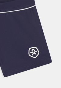 Navy swim shorts made of smooth, stretchy fabric. Features a white accent stripe and a hexagonal logo in white on the lower left.