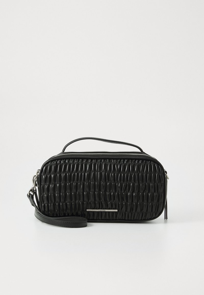 Sac à main rectangulaire en cuir noir avec texture froncée, fermeture éclair en haut, poignée fine et bracelet de poignet amovible sur fond blanc.