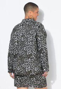 Giacca con stampa leopardata in tonalità di grigio e nero, con una vestibilità rilassata, dettagli con bottoni sulle maniche e cucitura della spalla sul retro.