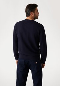 Granatowy sweatshirt z okrągłym dekoltem i długimi rękawami, wykonany z gładkiego materiału. W zestawieniu z ciemnymi dżinsami, z trójkątnym logo na tylnej kieszeni.