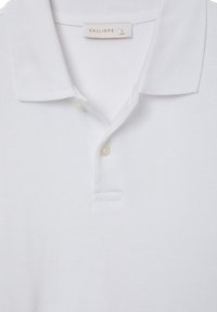 Weißes Poloshirt aus strukturiertem Stoff. Verfügt über einen klassischen Kragen, eine Knopfleiste und eine kleine geschlitzte Tasche in der Nähe der Knopfleiste.