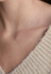 Primo piano di un maglione beige con texture e design a V, che mette in mostra un morbido materiale a maglia e sottili variazioni di colore e motivo.