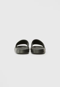 Svart slip-on sandaler med åpen bak. Laget av glatt, matt materiale. Rundet, polstret fotseng og teksturert såle for grep.