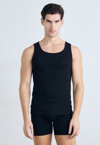 Schwarzes ärmelloses Tanktop aus glattem Stoff, mit rundem Ausschnitt und dezentem "BOSS"-Logo auf der linken Brust. Getragen mit schwarzen Shorts.