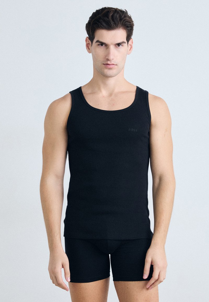 Schwarzes ärmelloses Tanktop aus glattem Stoff, mit rundem Ausschnitt und dezentem "BOSS"-Logo auf der linken Brust. Getragen mit schwarzen Shorts.