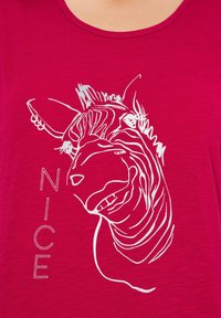 Fuchsiový tričko s bílým obrysovým grafikou hlavy zvířete a slovem "NICE" pod ním. Měkká textura, kulatý výstřih.