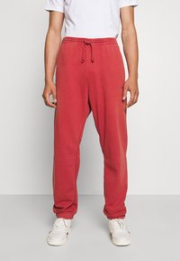 Röda träningsbyxor med resårmidja och dragsko, med sidofickor och smalnande muddar, som bärs med vita sneakers och en enkel t-shirt.