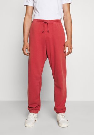 Rote Jogginghose mit elastischem Bund und Kordelzug, ausgestattet mit Seitentaschen und schmal zulaufenden Bündchen, getragen mit weißen Turnschuhen und einem schlichten T-Shirt.