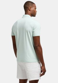 Shirt de polo verde menta claro con mangas cortas, textura suave y un cuello clásico. Combinado con pantalones cortos blancos texturizados, que presentan un patrón acolchado.