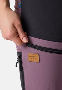 I pantaloni da esterno Swedemount presentano un design nero e viola, con una tasca con zip e un'etichetta in pelle color cuoio sul lato.