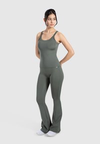 Zestaw oliwkowej zielonej koszulki na ramiączkach i rozszerzających się legginsów, uszyty z elastycznego materiału, z dekoltem w serek i minimalnymi detalami ściegów.