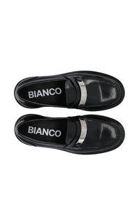 Mocassins en cuir noir avec une sangle brillante et un accent argenté, présentant une texture lisse et des semelles intérieures noires contrastantes marquées "BIANCO."