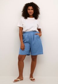 Light blue, textured shorts with an elastic waistband and side pockets, paired with a white t-shirt and neutral sandals.