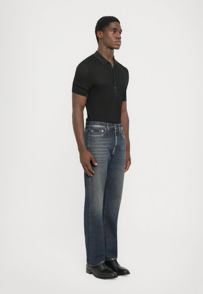 Black ribbed polo shirt, blue straight-leg jeans with faded texture, finished with black leather shoes, all displayed against a neutral background.