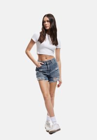 Farkkutrikoot, joissa on revitty helma ja korkea vyötärö, yhdistettynä slim fit -valkoiseen crop top -paitaan ja valkoisiin tennareihin, joissa on tekstuurisia yksityiskohtia.