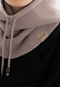 Gebreide sjaal in licht mauve, met een geribbelde textuur, een trekkoordsluiting met houten accenten, gedragen over een zwart kledingstuk.