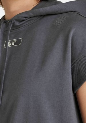 Ripresa ravvicinata di una persona che indossa un hoodie senza maniche grigio scuro con testo stampato bianco e lacci.