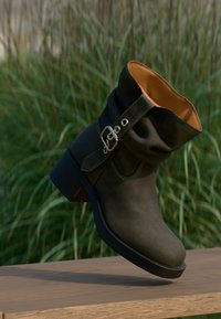 Stivale alla caviglia in pelle verde scuro con design morbido, accento con fibbia e texture liscia, dotato di un interno marrone e un tacco spesso.