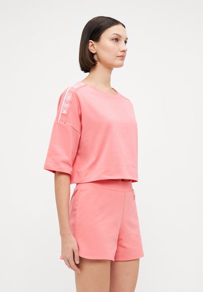 Pink cropped sweatshirt and shorts set in soft material. Sweatshirt features "Moschino" logo on sleeves; shorts have an elastic waistband.