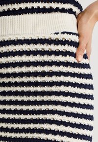 Stickad kjol i marinblått och krämvita ränder, med strukturerad mönstring och öppna stygn, samt en ribbad midja för en åtsittande look.