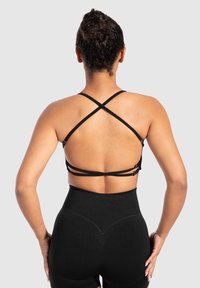 Zwarte sportbeha met gekruiste banden aan de achterkant, gemaakt van rekbare stof. Combinatie met zwarte high-waisted sportshorts.