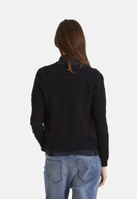 Námořnický pletený svetr s texturovanými vzory, kulatým výstřihem a dlouhými rukávy. V kombinaci se světle modrými džínami s detaily na zadních kapsách.