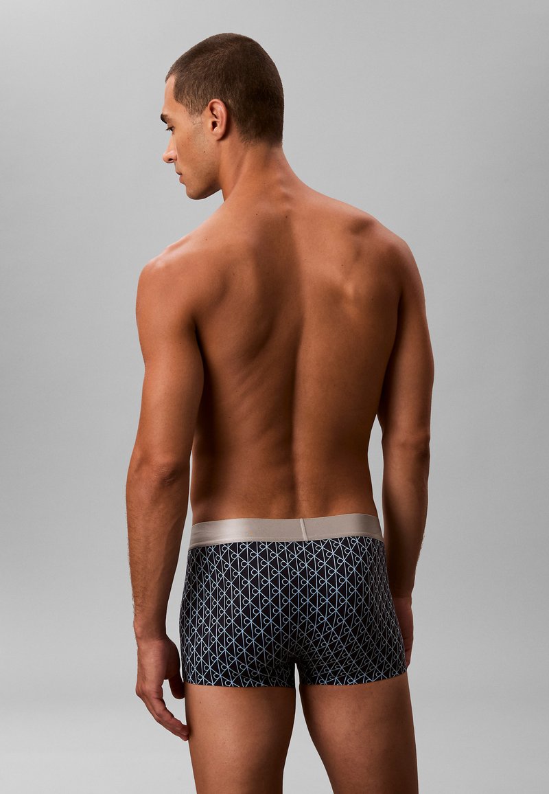 Bóxer negro con un patrón geométrico en azul claro, con una cinturilla suave en tono plateado. Textura suave, diseño ajustado.