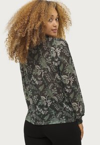 Bloemmotief blouse van doorzichtig zwarte stof met groene accenten, lange mouwen en elastische manchetten. Relaxte pasvorm met een ronde zoom.