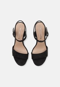 Sandales noires à bout ouvert avec brides à la cheville, semelles plates, et semelles intérieures beiges indiquant la taille 37 et la marque "Tamaris", vues de dessus.