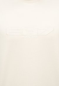 Λευκό ύφασμα με ανάγλυφο λογότυπο "EA7 Emporio Armani" στο κέντρο της περιοχής του στήθους.