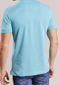 Polo en bleu clair, manches courtes, en coton doux, col standard, fentes latérales à l'ourlet, texture lisse, coupe décontractée.