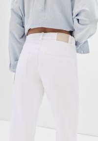 Beli denim hlače s zadnjimi žepi in teksturirano tkanino. Opremljene so s svetlo bež usnjenim označevalcem na pasu. V kompletu z modro črtasto srajco.