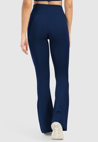 Leggings atletici a zampa di elefante blu navy con vita alta, realizzati in tessuto elasticizzato, caratterizzati da una texture liscia e calzature bianche a contrasto.